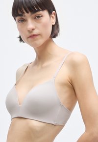 Ελαφρύ μπεζ σουτιέν με σχεδίαση σε σχήμα V, χωρίς ραφές στις θήκες, ρυθμιζόμενους ιμάντες και λεία υφή, με μινιμαλιστικό στυλ και διακριτικές ραφές.