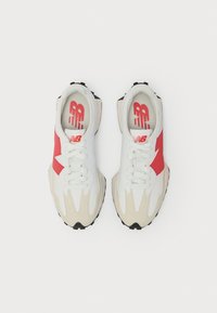 Białe i beżowe sneakersy z czerwonymi akcentami i sznurowadłami, widok z góry na jednolitym białym tle.