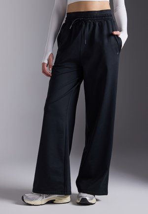Black wide-leg pants with an elastic waistband and side pockets, made from a soft material, paired with silver athletic shoes.