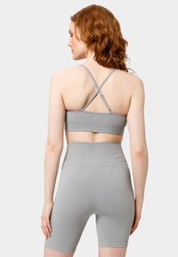 Šedá žebrovaná sportovní podprsenka a šortky s vysokým pasem a kříženými ramínky. Vyznačuje se hladkým, elastickým materiálem a přiléhavým střihem.