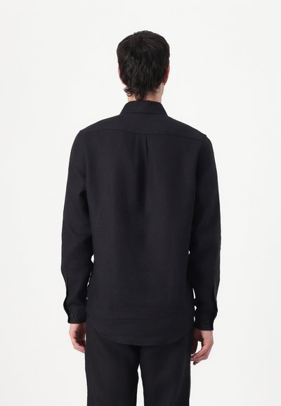 Chemise en lin noir à manches longues avec un col boutonné, une grande pli au dos et un ourlet arrondi. Dotée de poignets à un bouton et d'une texture mate.