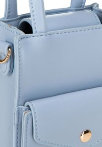 Borsa a tracolla in pelle azzurra chiara con texture liscia, accessori in oro, piccolo taschino frontale e manici corti. Forma rettangolare con dettagli cuciti.