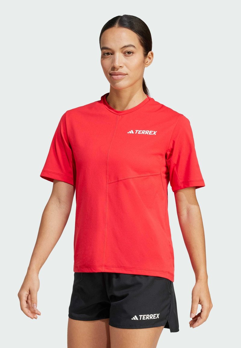 Röd kortärmad skjorta med rundad hals och detalj av framficka, ihop med svarta shorts med en vit "TERREX"-logga. Mjuk tygstruktur.