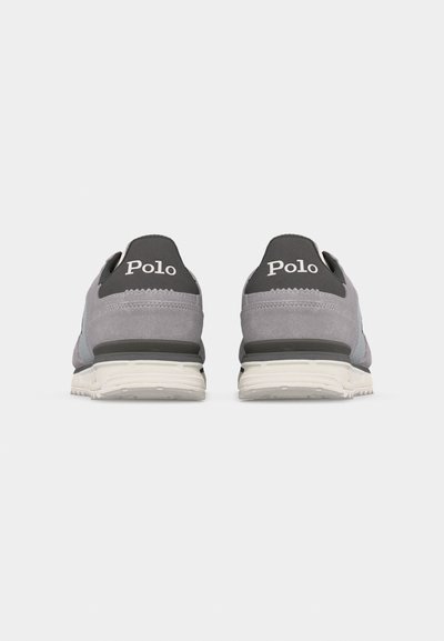 Par čevljev iz sivega semiša s belimi podplati, videnih od zadaj, z belimi črnimi obliži na petah z napisom "Polo".