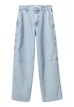 Personne portant un débardeur blanc, un jean bleu clair à jambes larges avec des poches avant et des ballerines en satin beige, debout avec une main dans la poche.