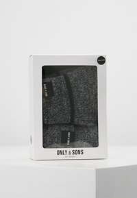 Two pairs of black and gray textured socks packaged in a transparent box with a black label. Brand name visible on the front. One size.