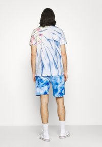 Chemise à manches courtes tie-dye bleue avec un motif tourbillonnant et des accents roses, associée à un short tie-dye bleu. Les deux articles ont une texture douce.