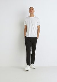 T-shirt blanc à manches courtes, pantalon noir et baskets blanches. Un tissu lisse, un design simple et une coupe décontractée créent un look informel.