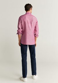 Roze linnen overhemd met lange mouwen, opgerolde manchetten en een gebogen onderkant, gecombineerd met donkerblauwe spijkerbroeken en witte sneakers.