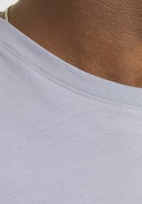 Camiseta de manga corta lila con una textura suave y un cuello redondo acanalado. Vista en primer plano del escote y la piel circundante.