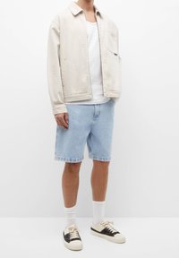 Lys beige jakke, hvid tanktop, lyseblå denim shorts, hvide ankelstrømper og sorte og hvide sneakers. Afslappet sommeroutfit.