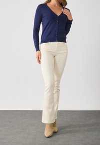 Tmavě modrý přiléhavý kardigan s výstřihem do V a zapínáním na knoflíky, kombinovaný s lehkými krémovými rozšířenými kalhotami a béžovými kotníkovými botami. Texturovaná látka.