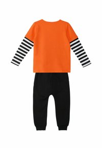 Orange Langarmshirt mit schwarz-weißen gestreiften Ärmeln, kombiniert mit schwarzen Hosen. Aus weichem, dehnbarem Stoff; lässiges Design.
