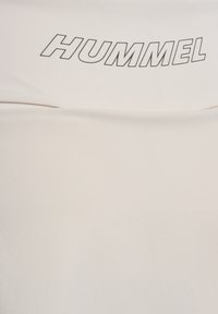 Ανοιχτό μπεζ T-shirt με μεγάλο μαύρο λογότυπο "HUMMEL" στο στήθος. Φτιαγμένο από μαλακό, λείο ύφασμα με άνετη εφαρμογή.