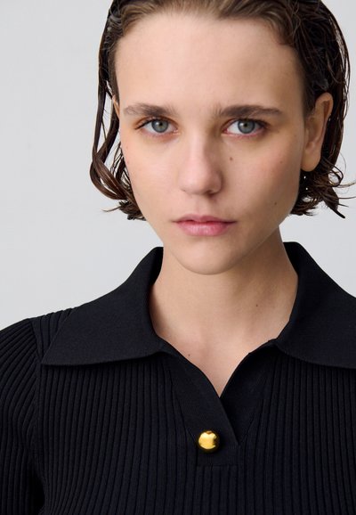 Polo shirt nero a coste con dettaglio dei bottoni, caratterizzato da un colletto classico e un tessuto testurizzato. La vista ravvicinata mette in evidenza il collo e la texture.