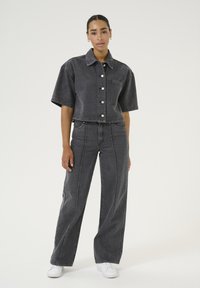 Black denim cropped shirt with short sleeves, featuring a front pocket and silver buttons, paired with high-waisted, wide-leg black jeans with seams.