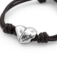 Pulsera de cuero en marrón oscuro con dos dijes de corazón plateados, uno grabado con "amor", presenta una textura suave y detalles anudados.