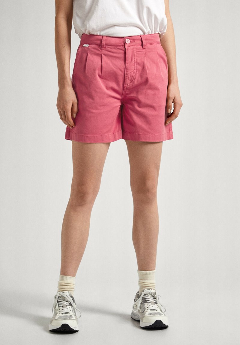 Pantaloni corti rosa in cotone con vita alta, pieghe e tasche laterali. Abbinati a sneakers neutre e calzini texture.