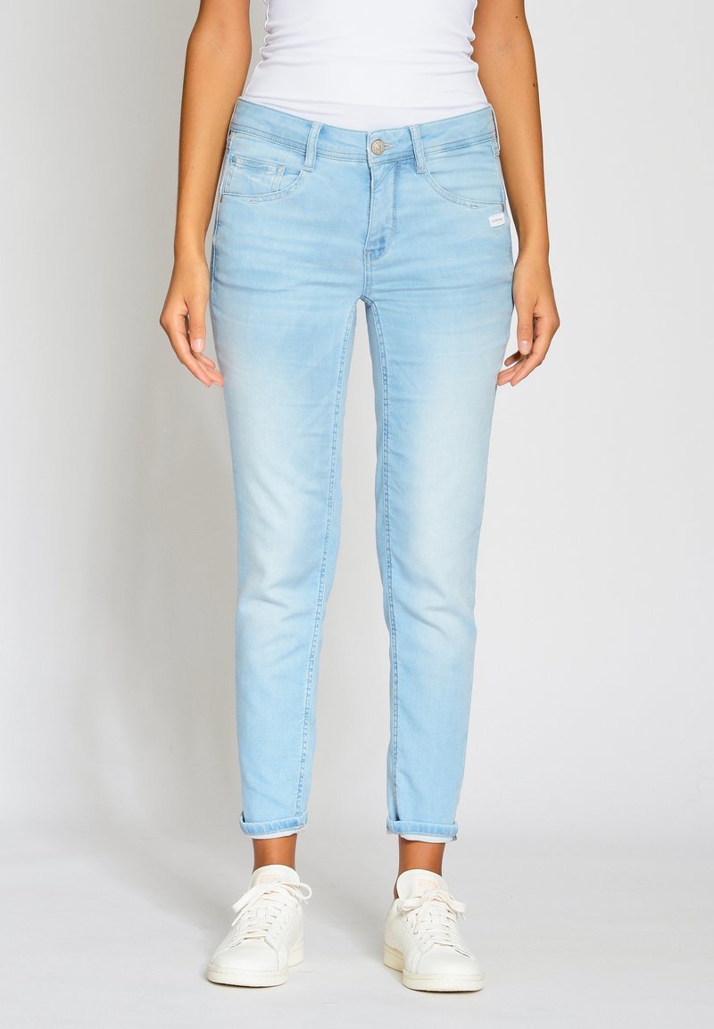 Vaaleansiniset farkut kapealla mallilla, viisi taskua ja napillinen suljin. Hihansuut kääritty nilkoissa, sileä pinta; rento tyyli.