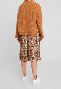 Gruby, prążkowany pomarańczowy sweter połączony z plisowaną spódnicą midi w zebrę i białymi sneakersami, podkreślając kontrastujące tekstury i wzory.