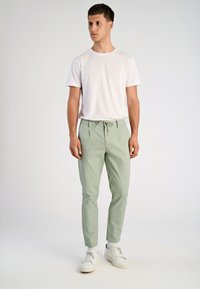 Chinos verde chiaro con vita regolabile, taglio slim e tasche laterali, abbinati a una t-shirt bianca a girocollo e sneakers bianche.