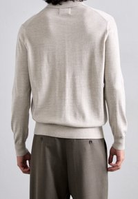 Pull en maille beige clair avec un col rond et des poignets côtelés. Il présente un ourlet ajusté et une texture subtile sur le tissu.