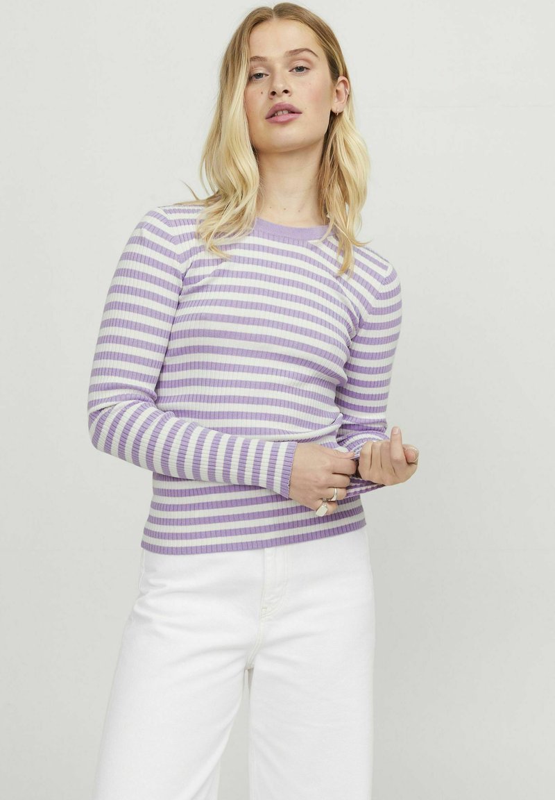Top de manga larga a rayas moradas y blancas con escote redondo y silueta ajustada. El modelo lleva pantalones blancos.
