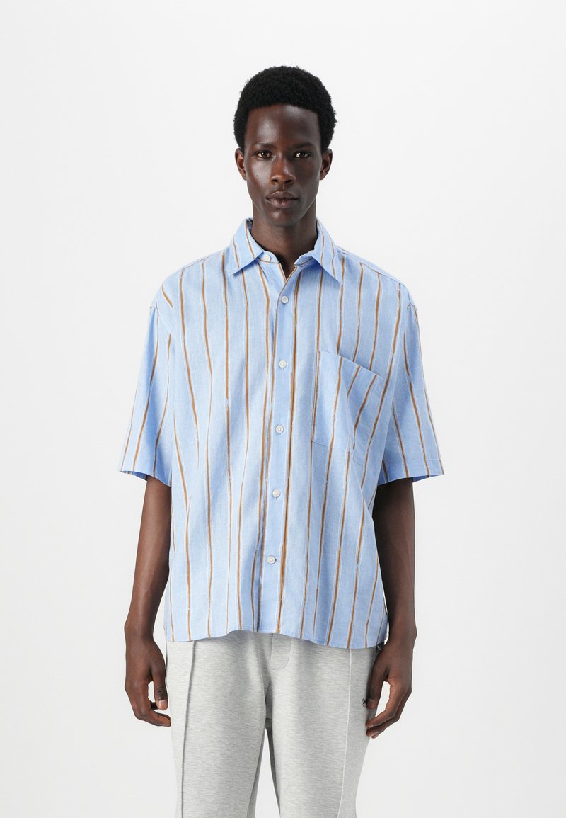Camisa de manga corta a rayas azules con rayas verticales marrones, con cuello abotonado y un bolsillo de parche en el lado izquierdo, hecha de una tela ligera.