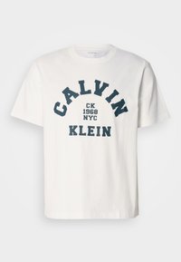 Valge puuvillane T-särk, millel on mereväe sinine tekst, mis ütleb "CALVIN KLEIN CK 1968 NYC," julge, kaarekujulise fondiga. Klassikaline ümar kaelus.