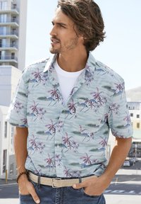 Camicia a maniche corte di colore azzurro chiaro con stampa tropicale di palme in rosa e verde. Presenta una tasca, un colletto e una chiusura con bottoni.
