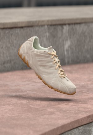 Beige sportssko med glatt mokkaskinn på overdelen, intrikate detaljer på siden, gummisåle og lys grønn innside, med beige lisser.