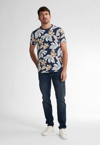 Laivastonsininen lyhythihainen t-paita, jossa valkoinen ja beige kukkakuvio, yhdistetty tummiin farkkuihin ja valkoisiin lenkkareihin. Rento istuvuus ja siistit linjat.