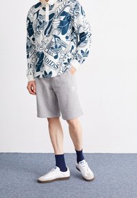 Vit och marinblå långärmad skjorta med grafisk design, i kombination med grå shorts och vita sneakers, som har blå detaljer och ankelsockor.