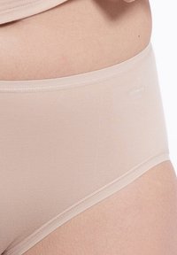 Nude damunderkläder gjorda av mjukt, stretchigt tyg med släta sömmar, med en låg midja och en diskret logotyp på sidan.