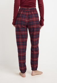Pantalones de pijama de cuadros en rojo y azul marino con cinturilla elástica y puños acanalados, que presentan una textura suave y un patrón a cuadros.