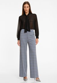 Blouse noire en dentelle avec un détail de cou noué, associée à un pantalon large taille haute en motif pied-de-poule bleu et blanc. Talons en argent.
