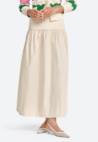 Beige Baumwoll-Maxikleid mit geraffter Taille und glatter Textur, kombiniert mit hellen Slingback-Schuhen mit spitzem Zehen.