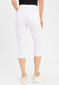 Weiße Cropped-Jeans mit umgeschlagenen Säumen, die über zwei Gesäßtaschen und eine glatte Textur verfügen, kombiniert mit beigen Sneakers.