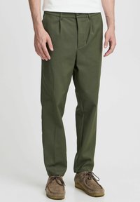 Pantalons plissés vert olive en tissu léger et lisse. Dispose d'une fermeture à bouton et à glissière, de poches latérales et d'une coupe ajustée.