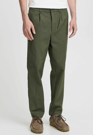 Pantalons plissés vert olive en tissu léger et lisse. Dispose d'une fermeture à bouton et à glissière, de poches latérales et d'une coupe ajustée.