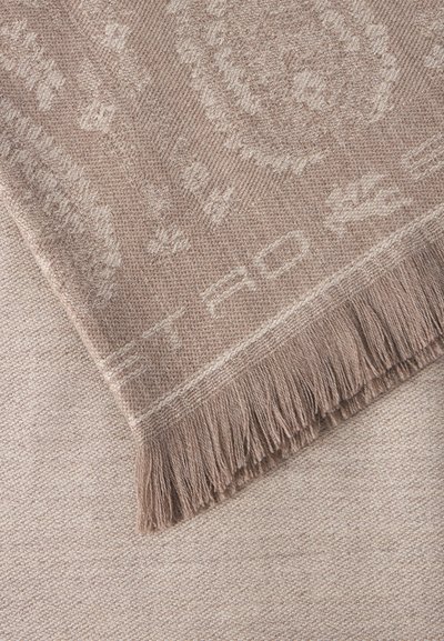Couverture tissée beige douce avec des motifs abstraits subtils et bord à franges, posée sur une surface texturée assortie.
