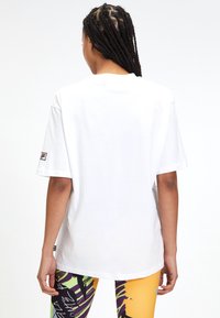 Vit oversized t-shirt i bomull, med rund halsringning och korta ärmar, prydd med en liten varumärkespatch på vänster ärm.