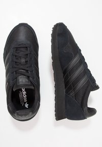 Mustat tennarit, joissa on yhdistelmä verkkokangasta ja mokkanahkaa, sivuilla kolme mustaa raitaa ja teksturoidut kumipohjat.