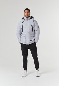 Light gray puffer jacket with a high collar, two zippered pockets, and black accents. Paired with black cargo pants and white sneakers.