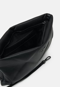 Borsa a tracolla in pelle nera con texture liscia, chiusura con zip, tasca interna e dettaglio logo impresso sul lato.