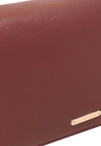 Rode leren portemonnee met een geribbelde textuur, voorzien van een goudkleurig metalen logoplaatje. Compact, rechthoekig ontwerp met scherpe randen.