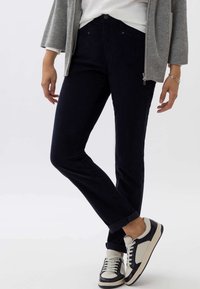 Navy corduroy broek met een slim fit, voorzien van een voorste knoopsluiting en opgerolde manchetten, gecombineerd met zwart-witte sneakers.