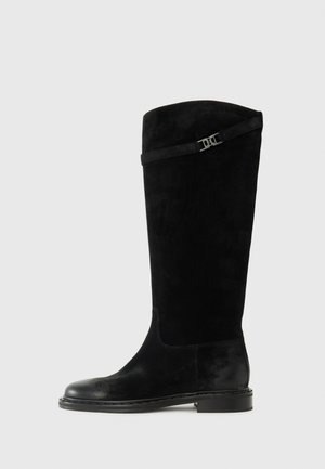 Bottes montantes en suede noir avec un bout rond, un talon plat et une sangle décorative avec une boucle en argent en haut.