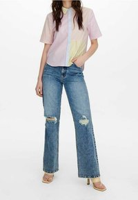 Chemise à manches courtes, boutonnée, en rose et rayures pastel, associée à un jean large déchiré bleu et des sandales à talons de couleur claire.