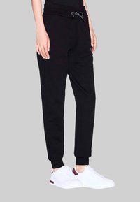 Zwarte joggers met een geribbelde tailleband en trekkoord, met zijzakken en taps toelopende boorden. Gecombineerd met witte sneakers.